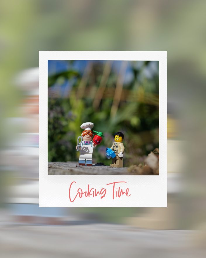 A Polaroid-style photo shows two LEGO figures: a chef holding kitchen utensils and a tomato, and a child holding a blue mixing bowl. Below them, Cooking Time is written in red. Blurred greenery is in the background.