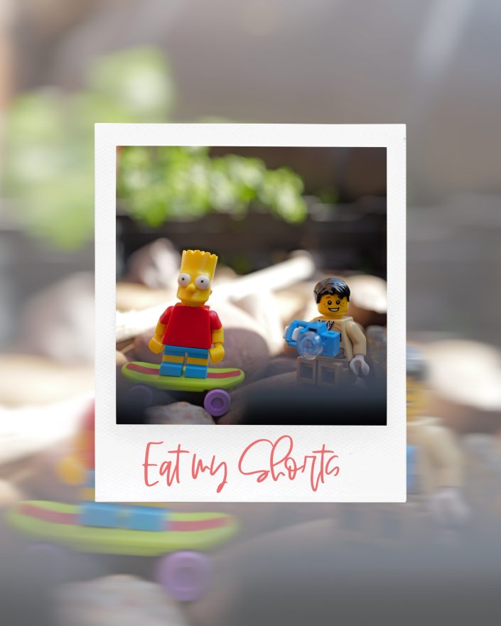 A Polaroid-style photo shows two LEGO figures: one resembling a boy on a skateboard and another holding a camera. The caption below the photo reads, Eat my Shorts in pink script.