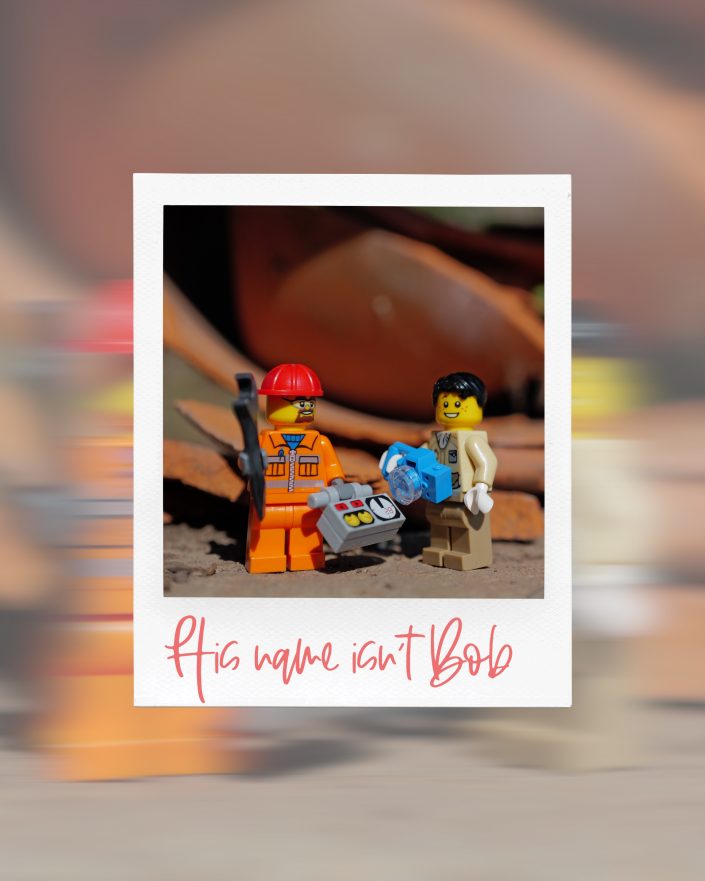 Two Lego minifigures stand facing each other; one wears an orange outfit and red helmet, holding a tool, whilst the other is in tan, holding a blue object. Text below reads, His name isn't Bob.