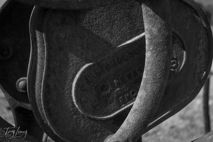 Close-up black and white photo of a weathered metal machinery part with embossed text, some of which reads S. HACKENSON and PEWAUKEE, WIS. Curved metal pieces frame the central panel.