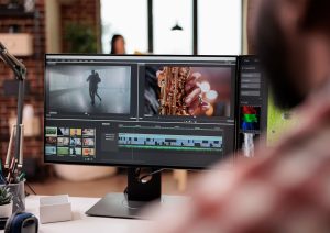 A computer monitor displays video editing software with multiple video clips, audio tracks, and editing tools visible, showing scenes of a dancing person, a saxophone player, and elements of photography layered into the project.