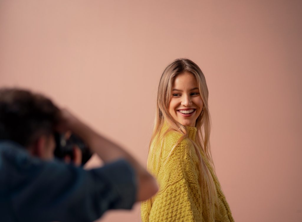 A young photographer taking pictures of model, backstage of photo shoot in studio.