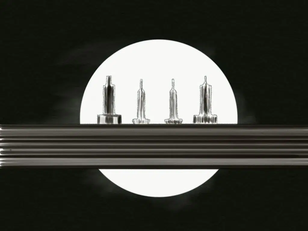 Four metallic machine parts stand upright on a horizontal metal surface, captured in striking photography and silhouetted against a large, bright white circle on a black background.