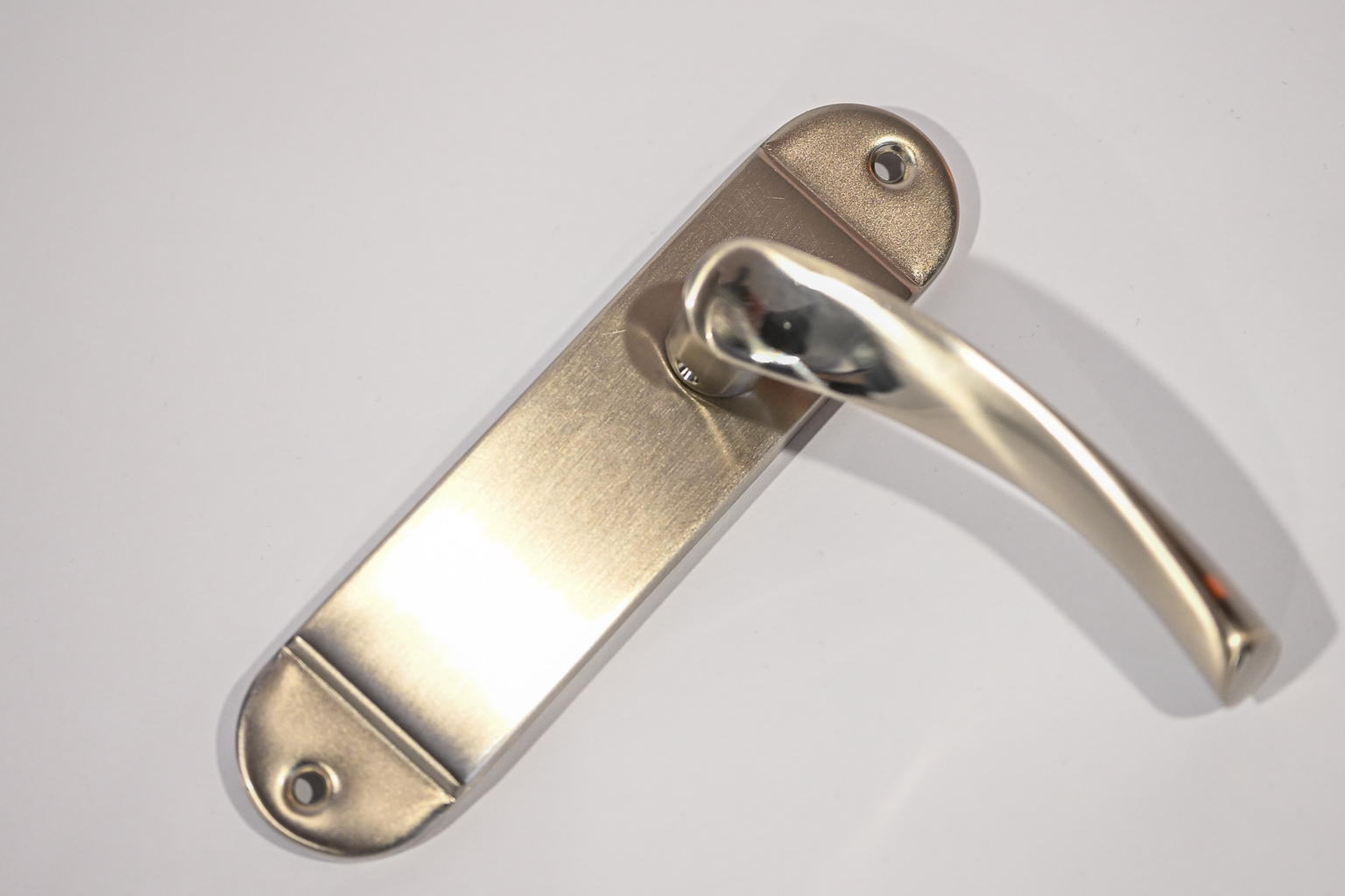 A close-up photography shot of a silver metal door handle attached to a rectangular backplate with two visible screws, set against a plain white background.