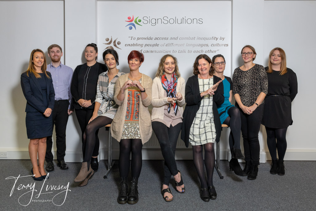 December - Sign Solutions employees pose smilingly for a group photo in front of a company sign inside an office.