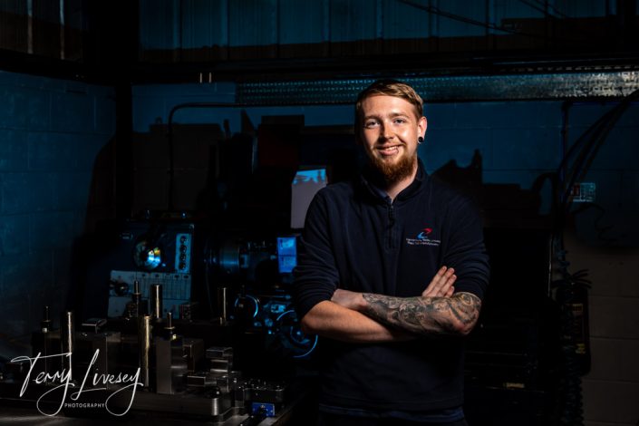 Canterbury Tools employee standing confidently with arms crossed in industrial workshop setting, machinery visible in background.