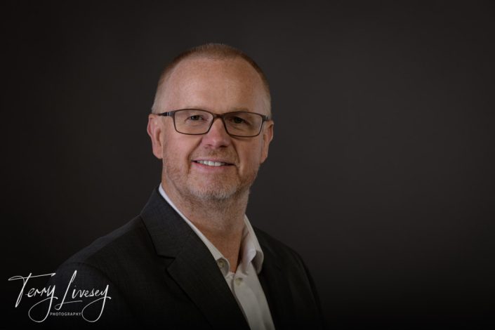 Intu Headshots professional headshot features a man wearing glasses and a suit against a neutral background.