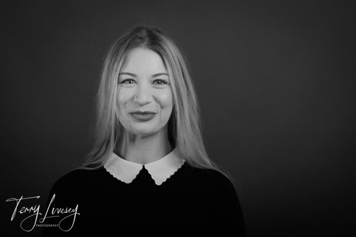 Intu Headshots portrays a woman with long hair wearing a dark top and white-collared shirt, facing camera.