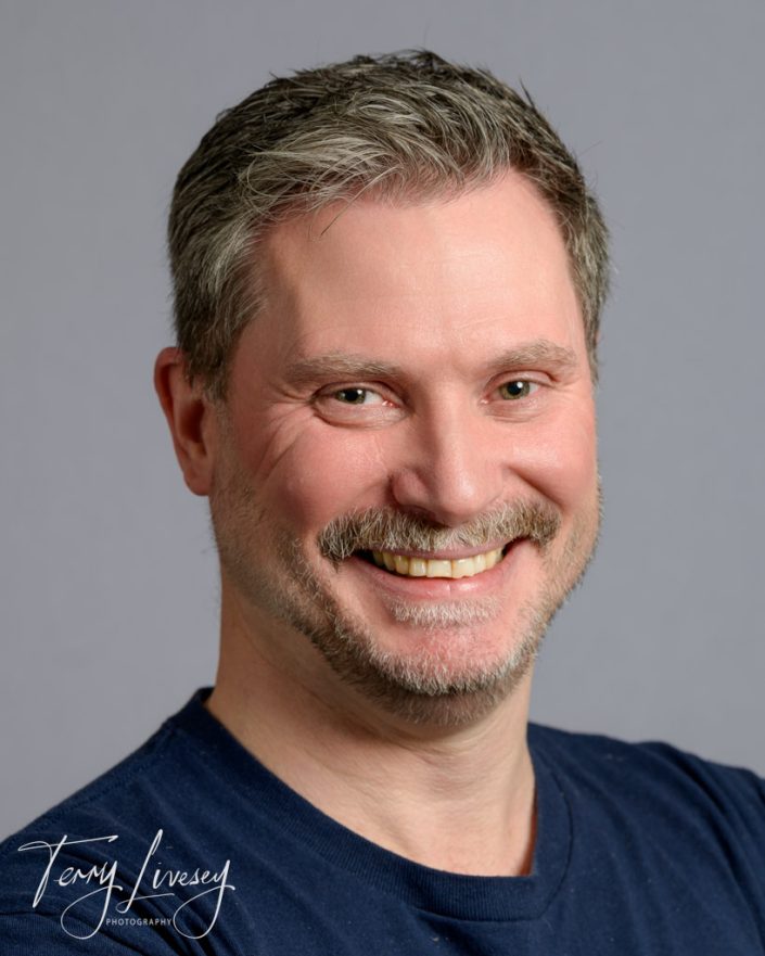 BMTC Headshots of a smiling man wearing a navy blue shirt against a plain background, suitable for professional use.