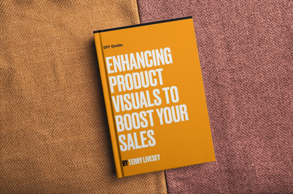 A book titled DIY Guide: Enhancing Product Visuals to Boost Your Sales by Terry Livesey rests on a textured surface with tan and pinkish fabric. The cover is bright orange with bold white and yellow text.
