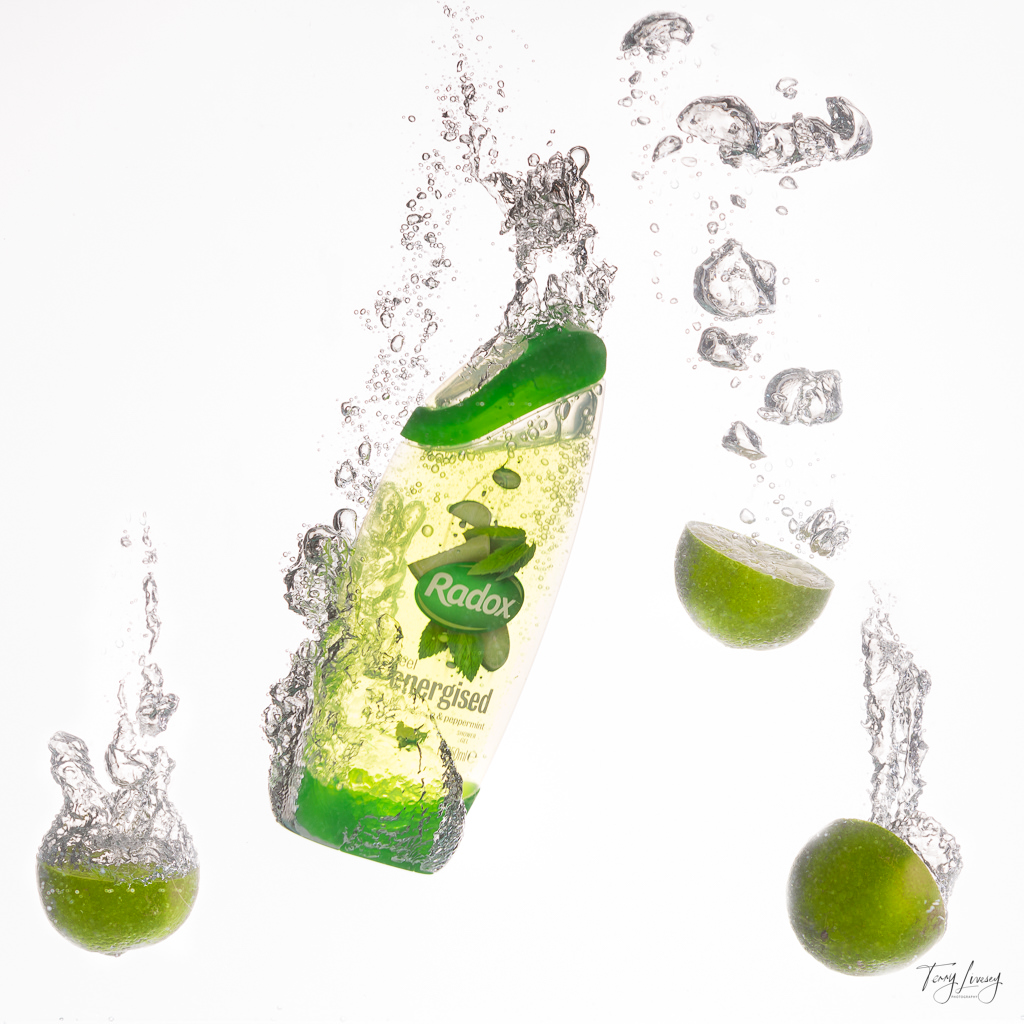 Studio photoshoot showing the Radox being dropped into a water tank. 3 limes are also in the show. Bubbles are rising to the surface around the products.
