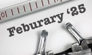 A close-up of a typewriter typing the words 25 Feburary (with a misspelling of February) on white paper, with part of the typewriter’s metal mechanism and a ruler visible.