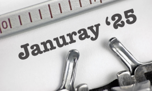 Close-up of a typewriter typing the words 25 January in bold text on white paper, with part of the typewriter’s metal typebars and ruler visible.