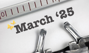 Close-up of a typewriter with the words 25 March and a yellow butterfly icon typed on white paper, with part of the typewriter's ruler visible at the top.