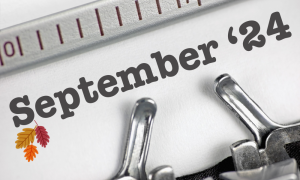 Close-up of a typewriter typing “September ‘24” on white paper, with two colourful autumn leaves illustrated in the lower left corner.