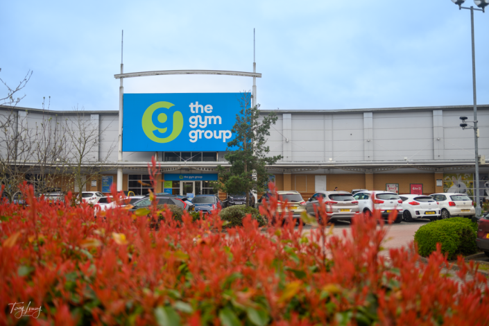 Shot through the hedge showing the Gym Group sign on Crossley Retail Park in Kidderminster