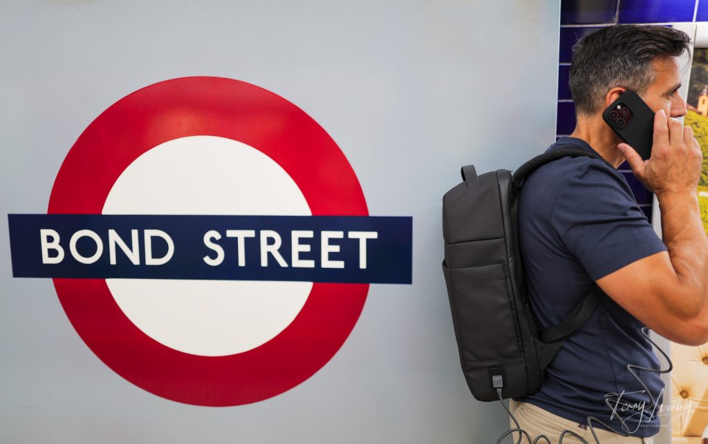 A male model using a phone next to the Bond Street tube logo in the station