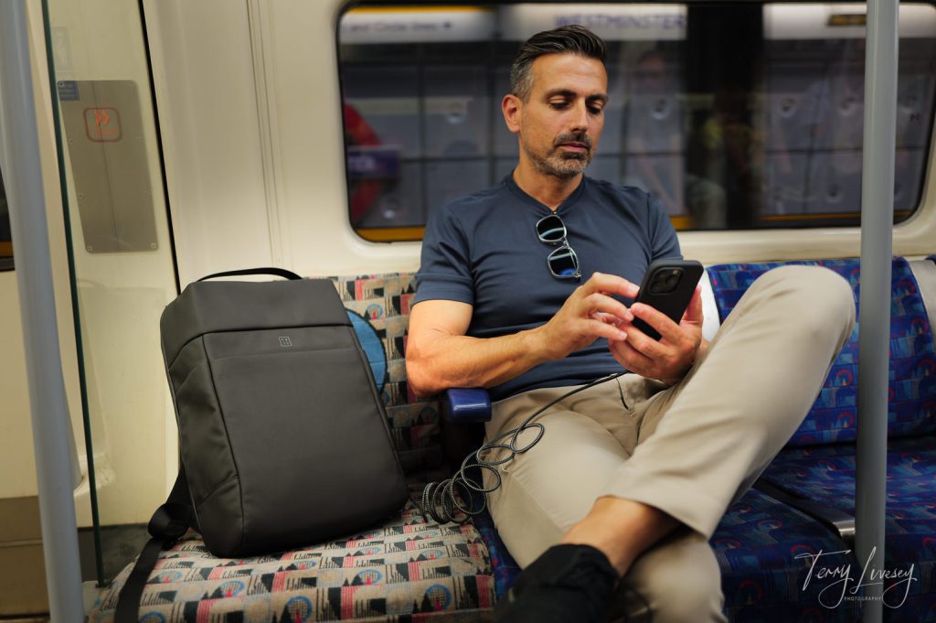 A male model using a phone next to PW3R backpack on a tube train in London