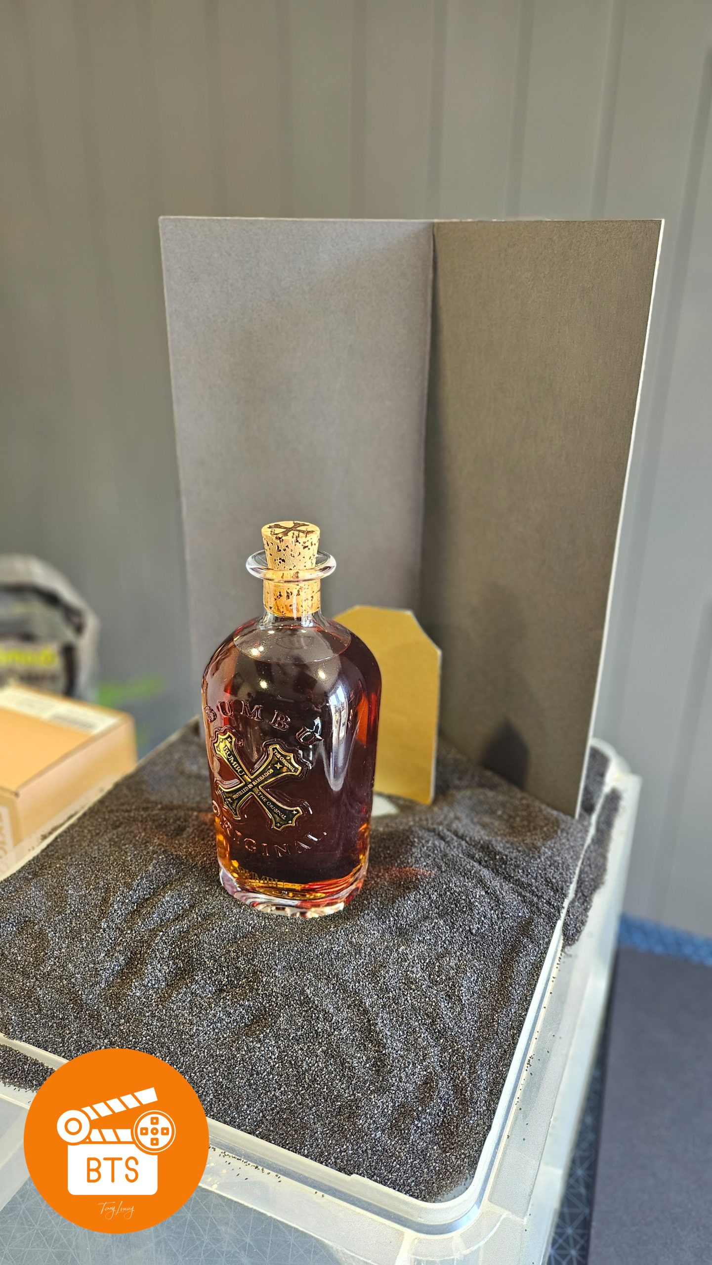 BTS shot of Bambu rum on a gravel base with a gold and black card in the background