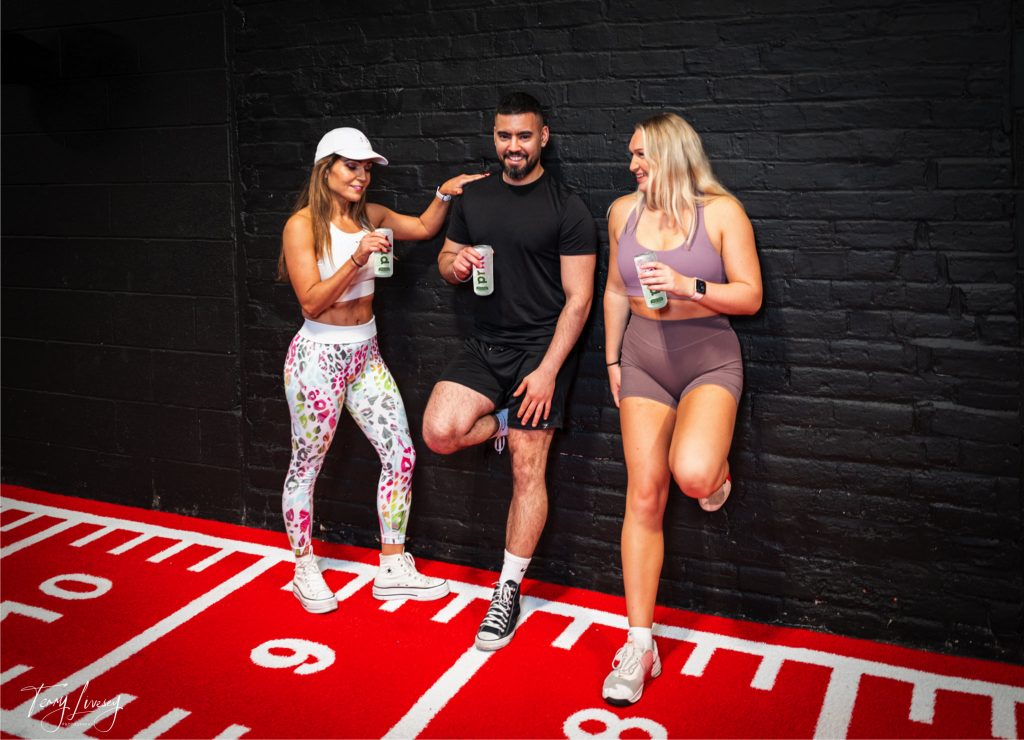 Gym shot of 2 women and 1 man with all drinking PRKL