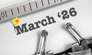 A close-up of a typewriter with the text 26 March and a yellow daffodil graphic next to March. A ruler is visible above the text.