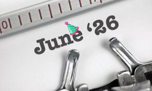 The text 26 June with a party hat graphic appears on a white page, partially under a typewriter bar and metal typewriter components.