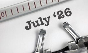 Close-up of a typewriter typing 26 July on white paper, with part of the typewriter's metal bar visible at the top.